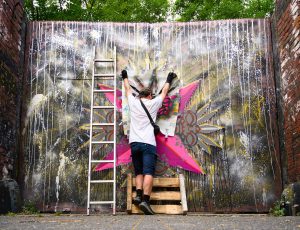 ErwaOne bei der Arbeit an seinem Streetart Werk in Köln Ehrenfeld. Farbenfrohe Gestaltung des Eingangstores der Künstlerkommune Kolbhalle. Urban Art