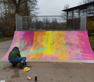 Streetart Workshop Landsberg Skatepark Neugestaltung Action-Painting, Teilnehmerin schlägt Farbsprühdose auf um die Farbe auf eine Skate-Rampe zu verteilen