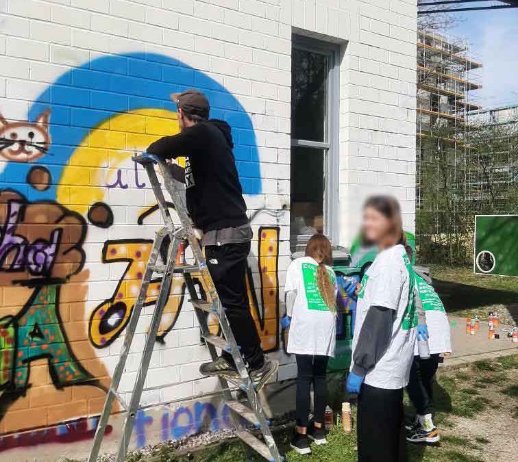 Graffiti Workshop im Jugendzentrum von Landsberg mit Ukraine-Flüchtlingen. Künstler ErwaOne auf Leiter an der Wand umgeben von teilnehmerinnen.