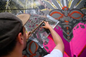 ErwaOne Urban Artist bei der Arbeit in Köln-Ehrenfeld, Nahaufnahme Künstler sprüht Schablone bunt