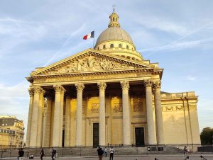 Gebäude beige Pantheon Paris erstrahlt im Abendlicht Menschen vor dem PLatz französische Flagge weht im Wind