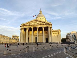Gebäude beige Pantheon Paris erstrahlt im Abendlicht Menschen vor dem PLatz französische Flagge weht im Wind