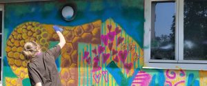 Ein Mädchen sprüht Farbe an eine Wand. Graffiti Workshop mit Erwa.One im Stellwerk Herrsching. Gemeinsames Graffito mit den Workshopteilnehmern