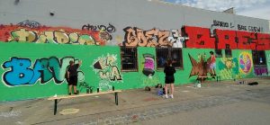 Jugendliche vor einer legalen Graffiti-Wand in Herrsching am Ammersee, Sprühworkshop mit Erwa.One und dem Haus der Jugend. Heißer Sommertag, grüner Hintergrund bunte Graffitis und streetart motive
