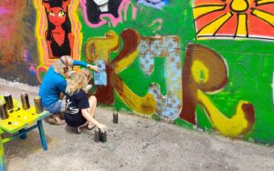 Eine Mutter sprüht mit ihrem Kind ein legales Graffiti an eine Wand während eines Graffiti- und Streetart Workshops in Ettringen.