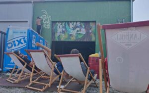 Bavarian Safari Graffiti Jam Landsberg 2023 Sem2 malt in 4 Meter Höhe einen Stier - erste Skizze, Auf Liegestühlen schaut das Publikum den Künstern bei der Arbeit zu