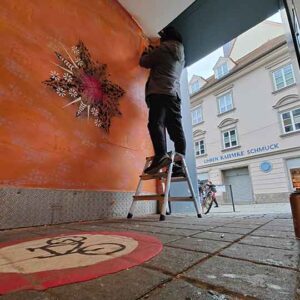 Streetart Projekt Neue Ornamente Neugestaltung Zederpassage / Galerieverein Landsberg, foto hamsterperspektive auf Künstler bei der Arbeit tagsüber, man kann aus der Passage in die Fußgängerzone der historischen Altstadt von Landsberg sehen, am Boden in Bodenfarbe gemalt - ein Fahrradverbotsschild für den Durchgang