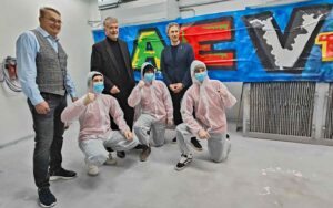 Die Nachwuchsspieler der Augsburger Panther beim Tag der offenen Tür der Handwerkskammer Schwaben in Augsburg bei einem Team-Foto mit den Vorständen. Drei erwachsene Männer im Hintergrund. Drei Jugendliche mit erhobenen Armen zur Faust, knieend und AEV-Graffiti im Hintergrund