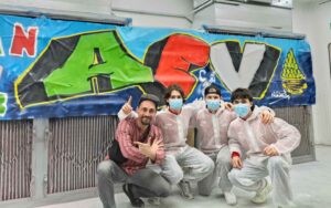Die Nachwuchsspieler der Augsburger Panther beim Tag der offenen Tür der Handwerkskammer Schwaben in Augsburg bei einem Team-Foto mit den Vorständen. Drei erwachsene Männer im Hintergrund. Drei Jugendliche mit dem Künstler, AEV-Graffiti im Hintergrund