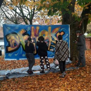 Demokratiebildung Bannergestaltung mit dem Jugendparlament von Ettringen Streetart Kunst Projekt mit Erwa.One und dem Kreisjugendring Unterallgäu Einführungssprühkurs Graffiti mit dem Wort "Demokratie" in bunten Farben, kunstpädagogische Vermittlung