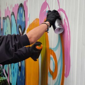 Zwei Personen besprühen eine Wand mit buntem Graffiti im Rahmen eines angeleiteten Workshops