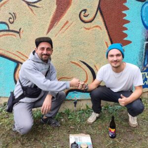 U27 Streetart-Stipendium Landsberg am Lech 2024. Erwa.One (Künstlerische Leitung) & Bjarne Jaschhof (Stipendiat) in Diessen am Ammersee. Im Hintergrund fertiges Streetart-Werk von Bjarne, welcher seine letzte Fläche im Rahmen des Stipenidums gestaltet hat.