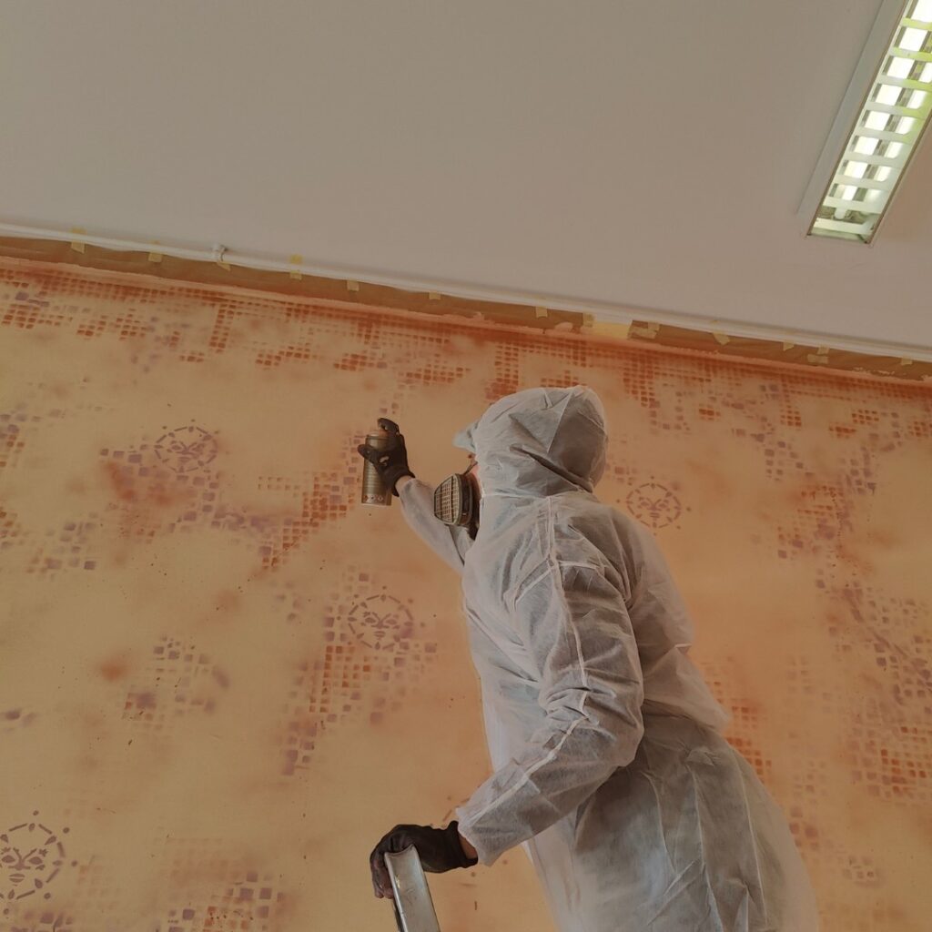 Künstlerische Auftragsarbeit Innenraumgestaltung durch Erwa.One. Der Künstler steht auf einer Leiter und sprüht an deinem pastel-organenen Hintergrund