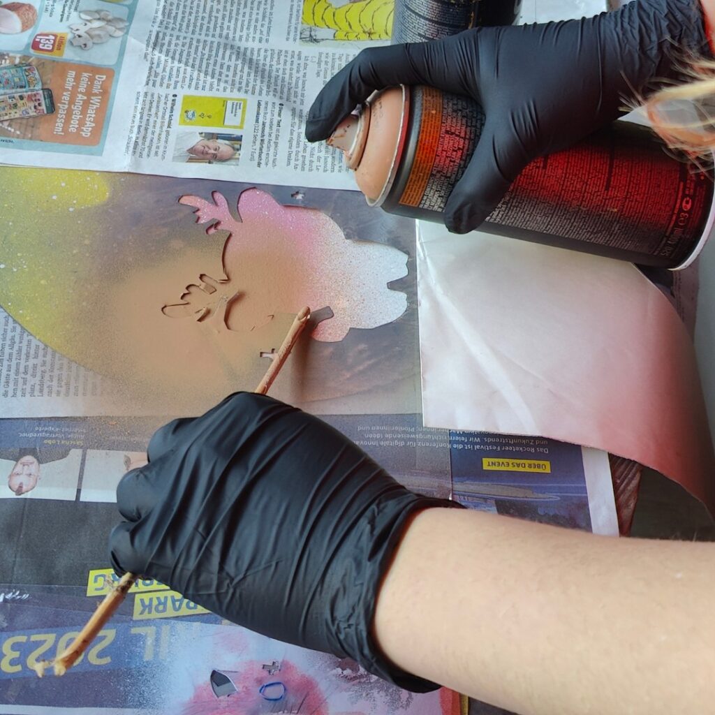 Sprüh-Workshop Urbane Kunst Methodik von ErwaOne an der Montessori-Schule von Kaufering. Ein Mädchen sprüht eine Schablone. Teil des Workshops zu Stencil-Kunst (wie Banksy, C215, ...)