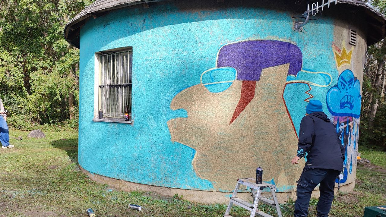 U27 Streetart-Stipendium 2024: Bjarne gestaltet einen illustrativen Graffiti Charakter auf das TrafoHaus der Ammerseewerke in der Riederau am Ammersee im Rahmen der Words for democracy Aktion mit dem Kreisjugendring und Streetwork