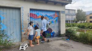 U27 Streetart-Stipendium Landsberg am Lech 2024: Gestaltung Garagentor Schondorf neben Realschule durch Stipendiatin Emma mit Interpretation eines Werkes von Caspar David Friedrich Wanderer im Nebelmeer klassiker der deutschen romantik. Kinder sind zugegen und sprechen mit der jungen Künstlerin