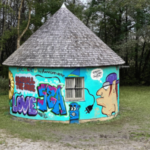 U27 Streetart-Stipendium Landsberg am Lech 2024: bunt gestaltetes Trafohaus der Ammerseewerke in der Riederau am Ammersee. Rechts ein CHarakter von Stipendiat Bjarne, links Gestaltungen von Jugendlichen im Rahmen des Words for democracy Projektes