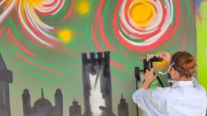 U27 Streetart-Stipendium Landsberg am Lech 2024: Stipendiatin Emma sprüht mit einer schwarzen Farbe eine Skyline auf eine Containerfläche am Papierbach