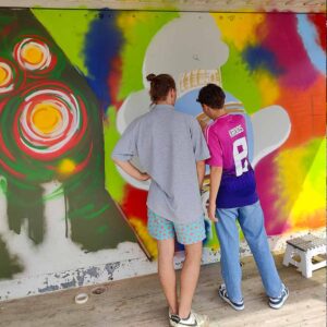 U27 Streetart Stipendium Landsberg am Lech Rückblick 2024: Bjarne Jaschhof sprüht eine COntainer-Innenfläche mit Streetart undeinem illustrativen Graffiti-Charakter sowie zeigt seinem Bruder das Sprühen. Concept by Erwa.One in Zusammenarbeit mit Kreisjugendring Landsberg