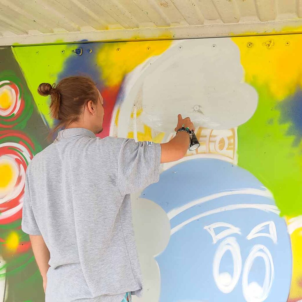 U27 Streetart Stipendium Landsberg 2024: Bjarne sprüht einen Charakter an eine Containerfläche vom Papierbach in Landsberg