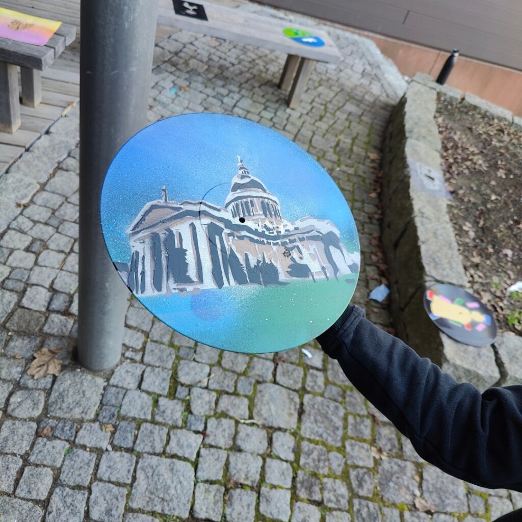 Sprüh-Workshop Urbane Kunst Methodik von ErwaOne an der Montessori-Schule von Kaufering. Ein junge zeigt sein Kunstwerk auf Schallplatte Vinyl