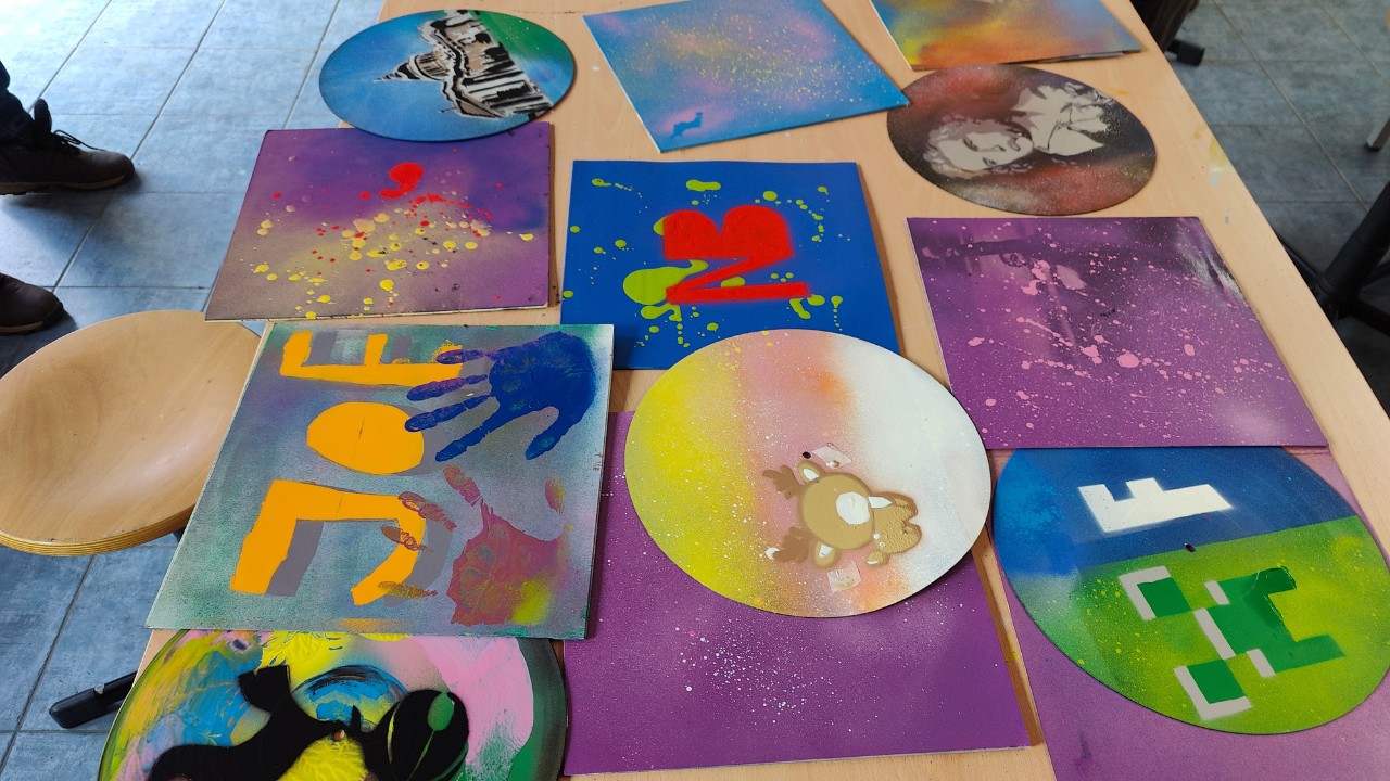 Sprüh-Workshop Urbane Kunst Methodik von ErwaOne an der Montessori-Schule von Kaufering. Die fertigen Kunstwerke auf Schallplatten und die dazugehörigen Cover liegen auf dem Tisch