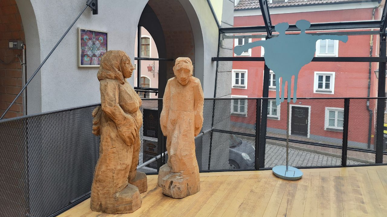 Kunstausstellung 90 Jahre Künstlergilde Landsberg-Ammersee-Lech im Stadttheater von Landsberg. Fine Art Print von ErwaOne im Obergeschoss begleitet von Holzskulpturen des Skulpteurs Oskar Imhoff aus Landsberg am Lech, Metall-Figur des Logos des Freundeskreis des Stadttheaters ist ebenfalls zu sehen