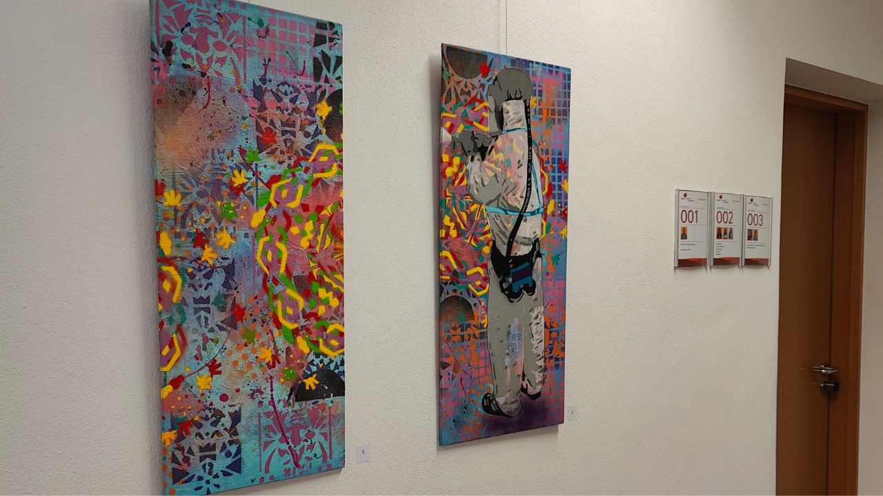 Viva la Buntness Graffiti & Streetart Ausstellung im Bürgerbüro von Aichach-Friedberg 2023. Zwei Werke auf Leinwand von ErwaOne bildende Kunst sind zu sehen. Daneben der Eingang in ein Büro der Behörde von Aichach