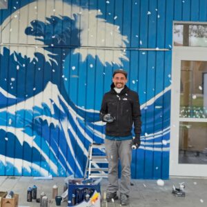 Streetart Künstler vor seinem fast fertigen Werk - einer modernen Interpretation der großen Welle vor Kanagawa von Hokusai an der Außenwand des Jugendzentrums Lechside Lounge
