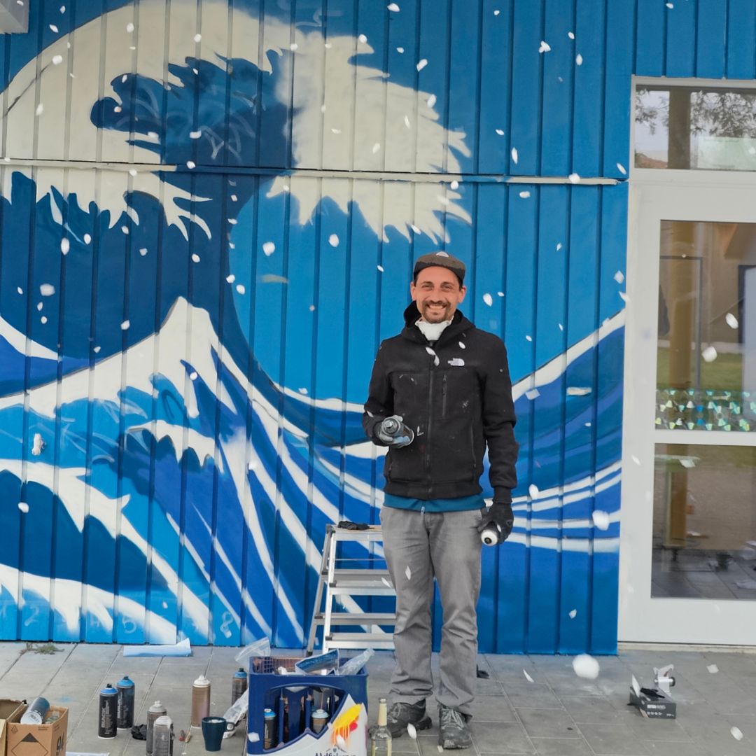 Streetart Künstler vor seinem fast fertigen Werk - einer modernen Interpretation der großen Welle vor Kanagawa von Hokusai an der Außenwand des Jugendzentrums Lechside Lounge