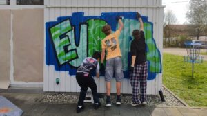Talentcampus Kaufering Kunstprojekt und Gestaltung des Jugendzentrums Lechside Lounge mit Jugendlichen zum Thema Europa, drei Workshop Teilnehmer sprühen ein gemeinsames Graffiti an die Wand