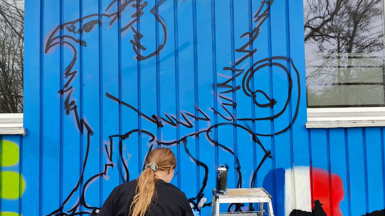 Talentcampus Kaufering Kunstprojekt und Gestaltung des Jugendzentrums Lechside Lounge mit Jugendlichen zum Thema Europa, eine Workshop-Teilnehmerin skizziert mit Sprühdose einen Greif an eine Wand mit blauem Hintergrund