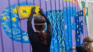 Talentcampus Kaufering Kunstprojekt und Gestaltung des Jugendzentrums Lechside Lounge mit Jugendlichen zum Thema Europa, ein Mädchen sprüht mit einer Schablone gelbe Sterne