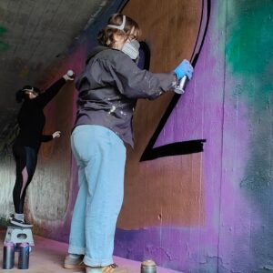 Zwei junge Frauen sprühen gemeinsam ein Graffiti an der legalen Sprühfläche von Landsberg