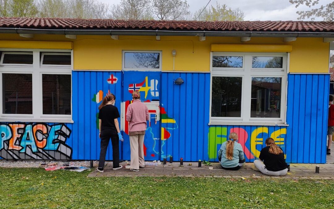 Talentcampus Kaufering Kunstprojekt und Gestaltung des Jugendzentrums Lechside Lounge mit Jugendlichen zum Thema Europa, Teilnehmer sprühen das Gebäude an, Graffiti mit Wort Peace / Frieden und Free, sowie europäischer Kontinent, vier junge Mädels arbeiten an ihren Wandbildern