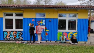 Talentcampus Kaufering Kunstprojekt und Gestaltung des Jugendzentrums Lechside Lounge mit Jugendlichen zum Thema Europa, Teilnehmer sprühen das Gebäude an, Graffiti mit Wort Peace / Frieden und Free, sowie europäischer Kontinent, vier junge Mädels arbeiten an ihren Wandbildern