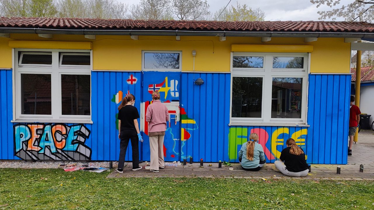 Talentcampus Kaufering Kunstprojekt und Gestaltung des Jugendzentrums Lechside Lounge mit Jugendlichen zum Thema Europa, Teilnehmer sprühen das Gebäude an, Graffiti mit Wort Peace / Frieden und Free, sowie europäischer Kontinent, vier junge Mädels arbeiten an ihren Wandbildern