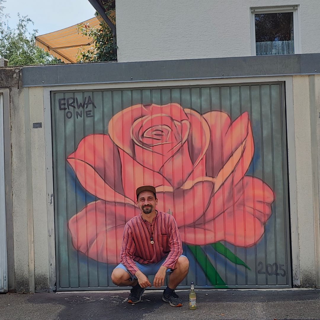 Streetart Künstler Erwa.One vor einem bunt gestalteten Garagentor.