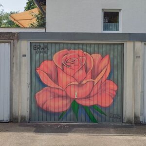 Bunt gestaltetes Garagentor in Landsberg am Lech, Oberbayern Deutschland. Streetart-Motiv Rose in rosé-Farbtönen. Ein Haus im Hintergrund mit Terasse. Sommer