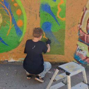 Intergenerationeller Streetart- und Graffiti Workshop mit ErwaOne in Landsberg am Lech an der legalen Sprühfläche der Stadt. Ein Junge sprüht einen Buchstaben und malt die innereFLäche aus