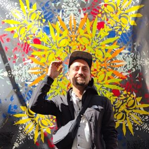 Künstler ErwaOne vor seinem Klangraum-Ornament Werk. Er hebt die rechte Hand leicht zum Kopf und lächelt.