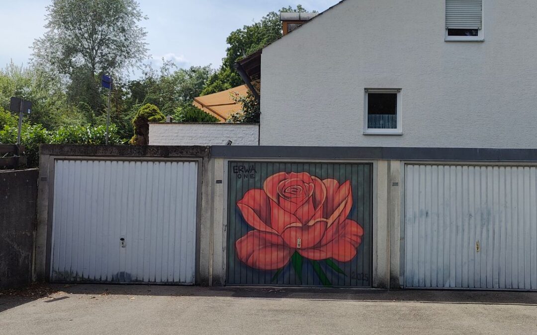 Bunt gestaltetes Garagentor in Landsberg am Lech, Oberbayern Deutschland. Streetart-Motiv Rose in rosé-Farbtönen. Ein Haus im Hintergrund mit Terasse. Sommer