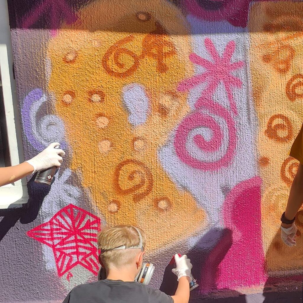 Graffiti- und Streetart Workshop mit Erwa.One in Herrsching am Ammersee. Mehrere Teilnehmer sprühen Peace an die Wand