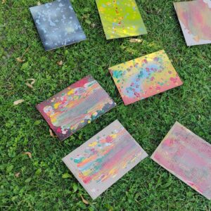 Streetart- und Graffiti Workshop im Rahmen des Ferienprogrammes des Jugendzentrums von Kirchheim an der Grund- und Mittelschule. Bunt besprühte Kartone liegen auf einer Wiese