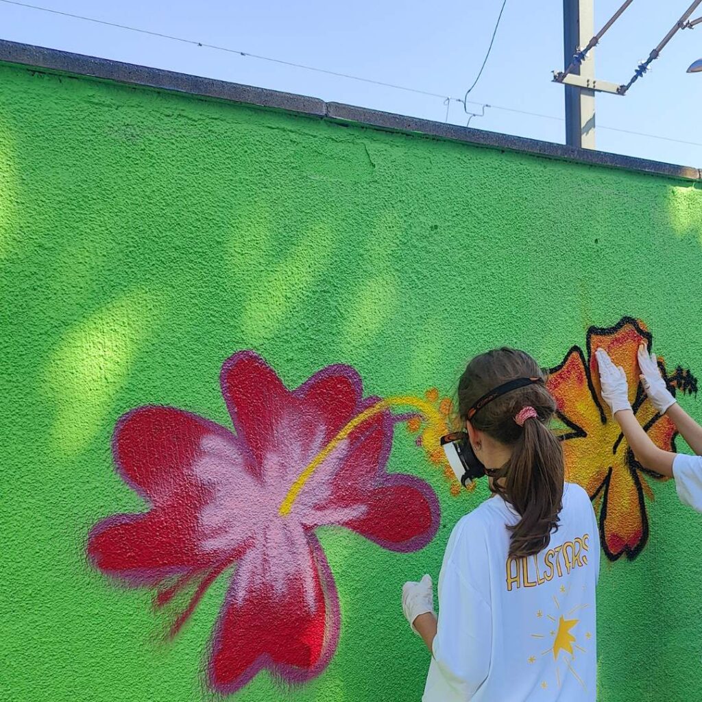 Graffiti- und Streetart Workshop mit Erwa.One in Herrsching am Ammersee. Zwei junge Mädchen sprühen auf einer grün grundierten Wand Blumen-Motive.