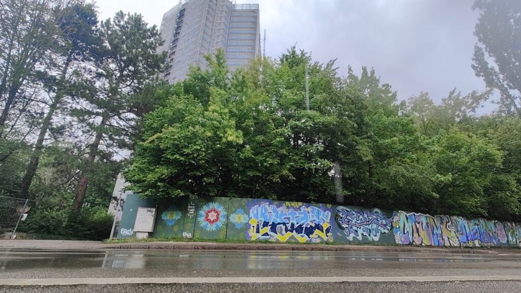 Peace Tower Jam am zukünftigen Studentenwohnheim Lechbrücke in Augsburg. Streetart und Graffiti auf Bauzäunen sorgen für Farbe und Miteinander. Der Turm ragt im Hintergrund in die Höhe.