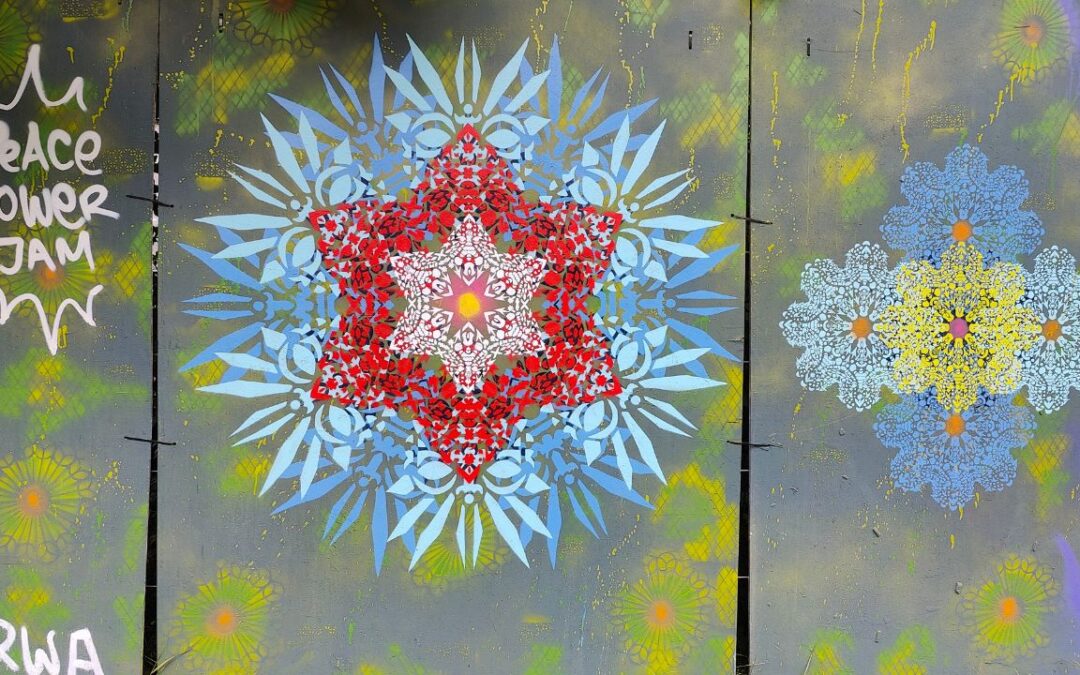 Peace Tower Jam am zukünftigen Studentenwohnheim Lechbrücke in Augsburg. Streetart und Graffiti auf Bauzäunen sorgen für Farbe und Miteinander. Das Kunst Konzept neue Ornamente ist auf dem Bild in blau und rot zu sehen und filigranen Schablonen. In der mitte ein roter Stern umgeben von blauen blüte-ähnlichen Motiven