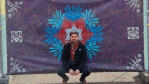 Der Künstler ErwaOne kniet vor seinem Kunstwerk "Ornament Waisenhausplatz" in Pforzheim. Er lächelt in die Kamera.