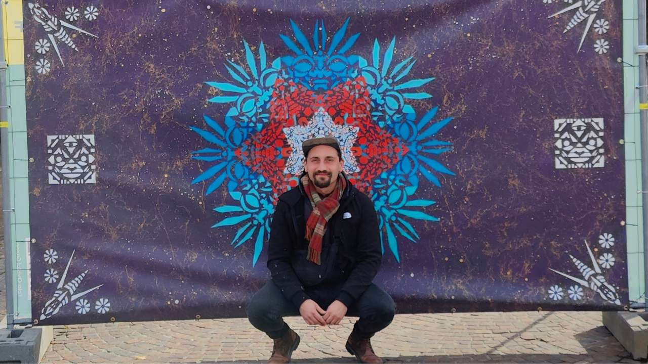 Der Künstler ErwaOne kniet vor seinem Kunstwerk "Ornament Waisenhausplatz" in Pforzheim. Er lächelt in die Kamera.