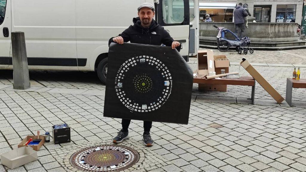 Streetart Künstler zeigt in Mindelheim einen abgedruckten Gulli-Deckel während seiner Print-the-City Intervention KulTOURtage Mindelheim Unterallgäu